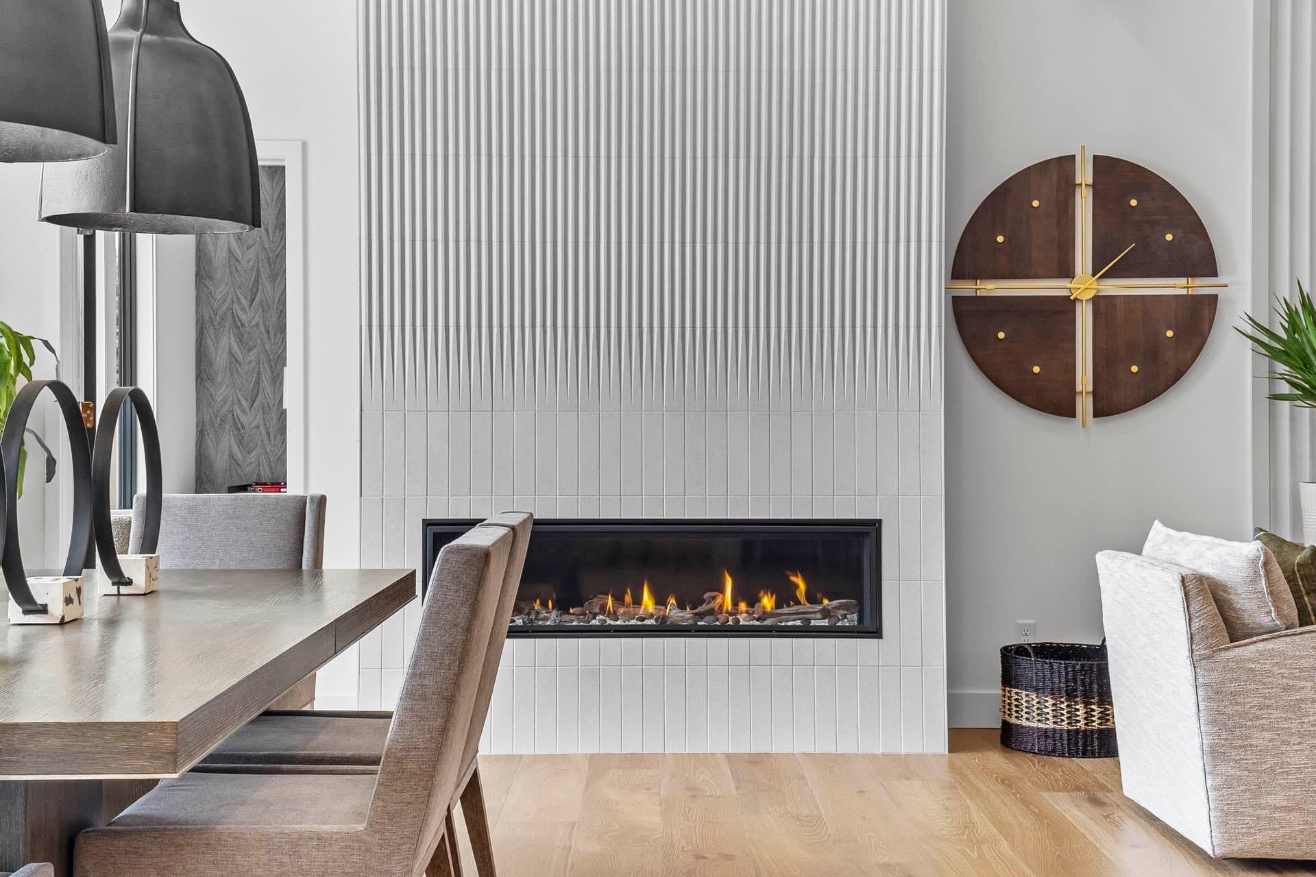 Dining area beside a fluted linear fireplace under a round wood clock