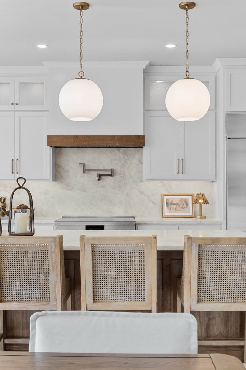 Kitchen island with globe pendants, a wood range hood and cane barstools